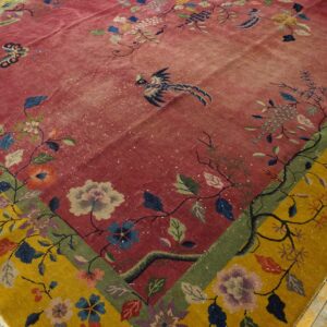 Ornate low-pile rug with a rose red field and mustard yellow floral border displaying birds on wood floors.