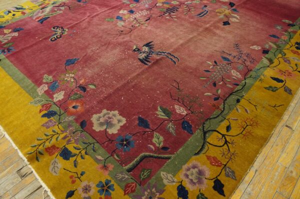 Ornate low-pile rug with a rose red field and mustard yellow floral border displaying birds on wood floors.