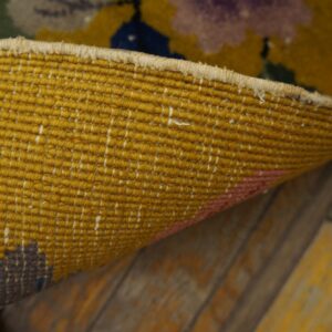 The golden-yellow backing of a woven rug is curled to reveal colorful patterns on rustic wood floors.