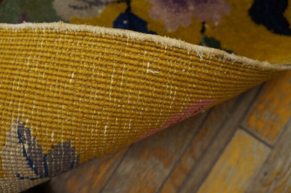 The golden-yellow backing of a woven rug is curled to reveal colorful patterns on rustic wood floors.