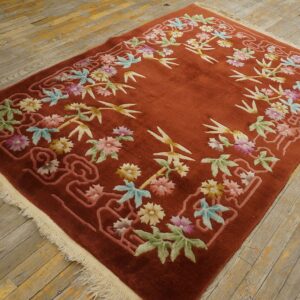 A rust-colored rug with sculpted colorful floral and bamboo motifs rests on weathered wooden floors.