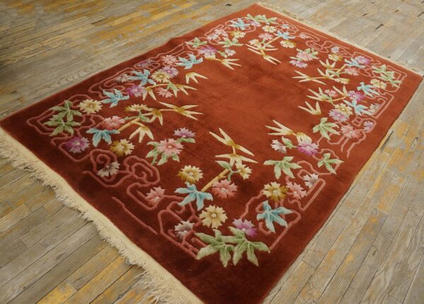 A rust-colored rug with sculpted colorful floral and bamboo motifs rests on weathered wooden floors.