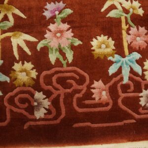 Velvety rust rug detailed with pink, yellow, and green flowers, bamboo, and a salmon-colored scrolling border.