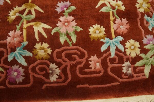 Velvety rust rug detailed with pink, yellow, and green flowers, bamboo, and a salmon-colored scrolling border.