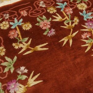 Close view of a high-pile red rug featuring pink, blue, and yellow floral designs on wood floor.