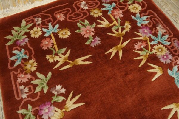 Close view of a high-pile red rug featuring pink, blue, and yellow floral designs on wood floor.
