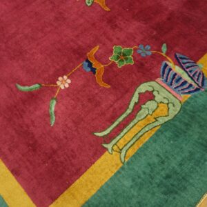 Magenta and green patterned rug corner with a yellow stripe rests on distressed wood flooring.