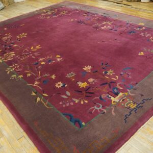 Magenta field rug with a dark brown border and detailed multicolored floral designs on wood planks.