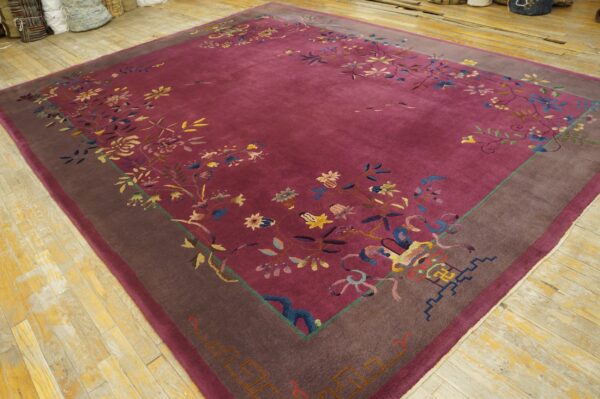 Magenta field rug with a dark brown border and detailed multicolored floral designs on wood planks.