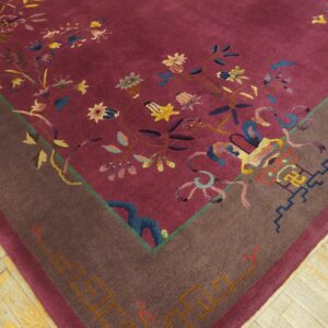 A close-up view of a magenta rug with multicolored floral patterns and a wide brown border, placed on light wood flooring.