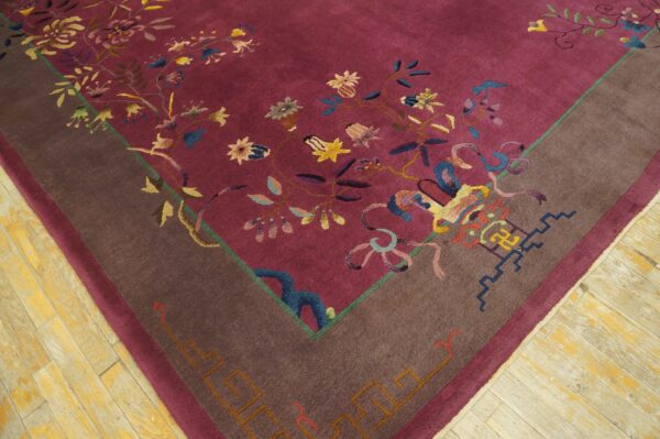 A close-up view of a magenta rug with multicolored floral patterns and a wide brown border, placed on light wood flooring.