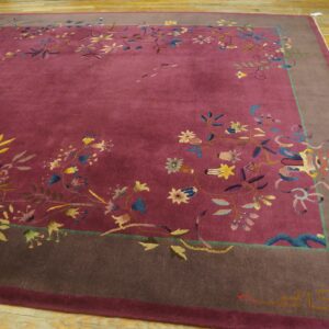 A deep magenta rug featuring colorful vines and flowers is framed by a wide taupe border on wood floors.