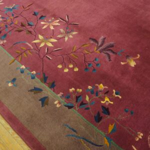 Close-up of a deep magenta rug featuring colorful floral vines and a wide brown border on wood planks.