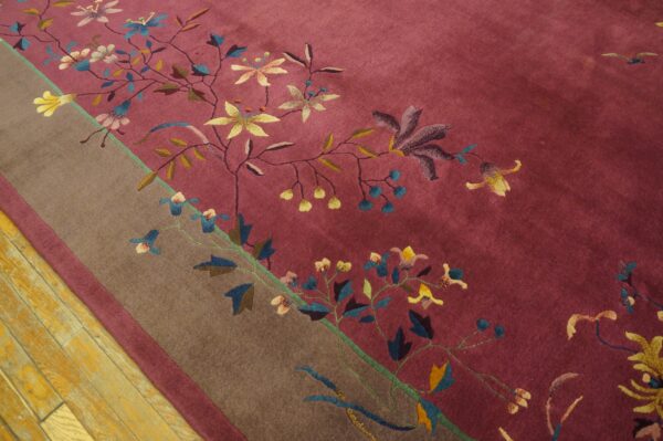 Close-up of a deep magenta rug featuring colorful floral vines and a wide brown border on wood planks.