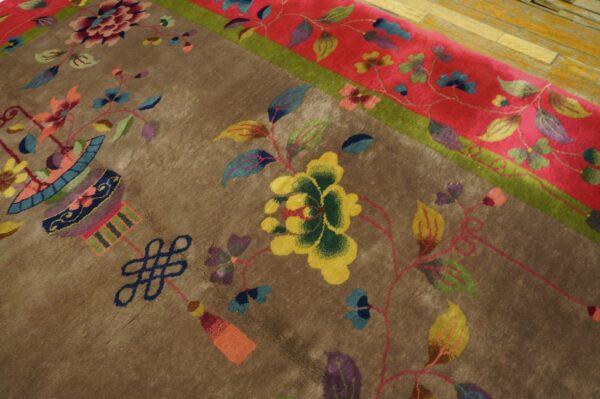 Plush brown rug with multicolored floral and knot motifs, framed by a red border next to wood plank flooring.