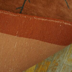Close-up of a reddish-brown rug edge showing ribbed backing and visible low pile on distressed wood flooring.