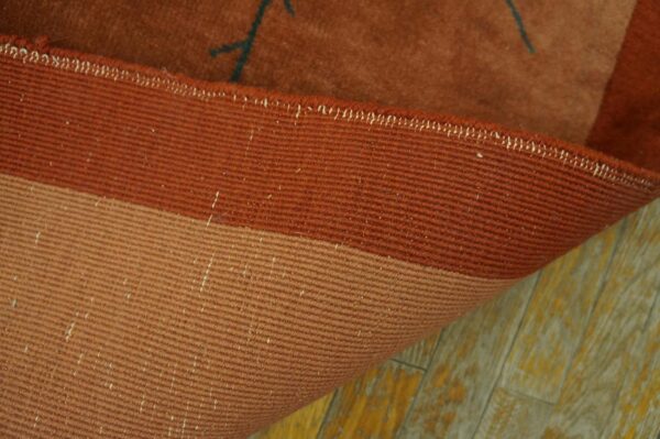 Close-up of a reddish-brown rug edge showing ribbed backing and visible low pile on distressed wood flooring.