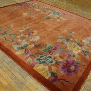 A salmon-colored rug featuring large scattered pastel floral designs rests on distressed light wood plank flooring.