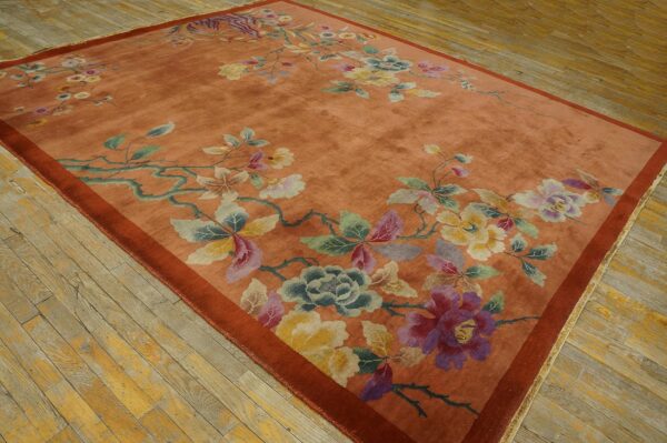 A salmon-colored rug featuring large scattered pastel floral designs rests on distressed light wood plank flooring.