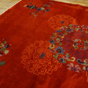 Close view of a deep red rug featuring multicolored floral sprays and tone-on-tone geometric motifs on a wood floor.