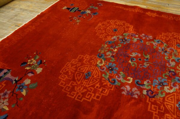 Close view of a deep red rug featuring multicolored floral sprays and tone-on-tone geometric motifs on a wood floor.
