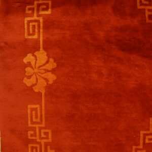 Deep reddish-orange rug with an orange geometric floral border shown next to light hardwood planks.