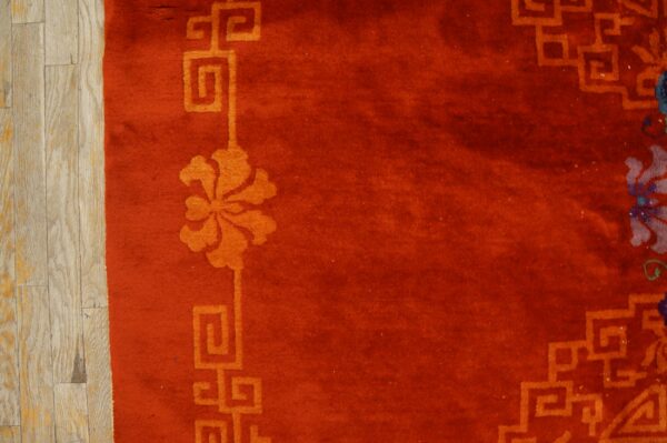 Deep reddish-orange rug with an orange geometric floral border shown next to light hardwood planks.