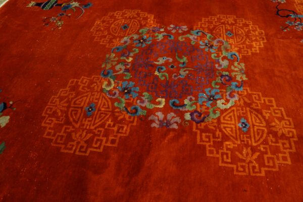 Deep red rug with high pile featuring a central multicolored floral medallion and geometric fretwork.