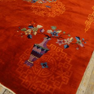 Bright red plush rug with a multicolored vase and floral design lies next to pale wooden flooring.