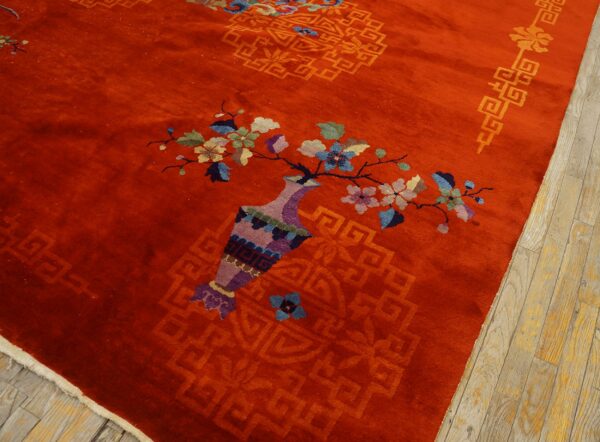 Bright red plush rug with a multicolored vase and floral design lies next to pale wooden flooring.