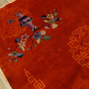 Multicolored floral and vase designs accent a high-pile red rug lying on light wood floors.
