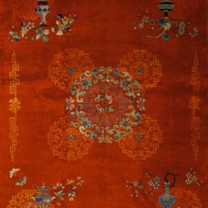 A rust-colored rug features ornate vases, pastel floral vines, a central medallion, and gold geometric borders.