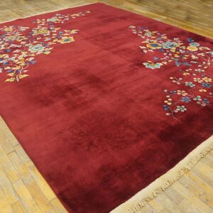 Deep red, high-pile rug with colorful blue and yellow floral motifs rests on distressed wood flooring.