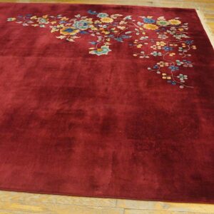 Deep red low-pile rug with colorful asymmetrical floral patterns sits on a wooden floor.