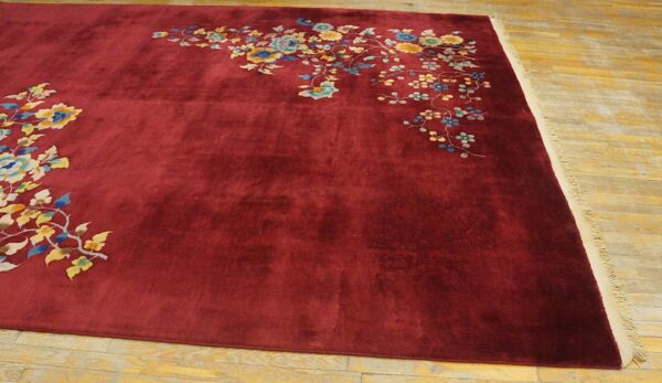 Deep red low-pile rug with colorful asymmetrical floral patterns sits on a wooden floor.