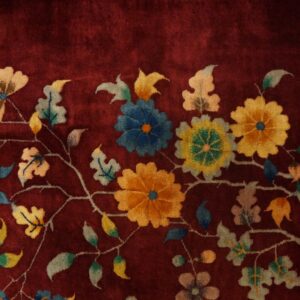 Close-up of a plush burgundy rug featuring yellow and blue blossoms and vines on distressed wooden floors.