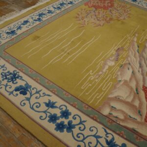 Scenic yellow-green rug featuring pink mountains and blue floral borders rests on rustic wood floors.