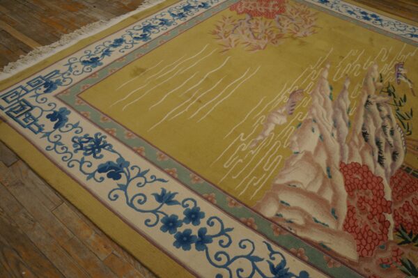 Scenic yellow-green rug featuring pink mountains and blue floral borders rests on rustic wood floors.