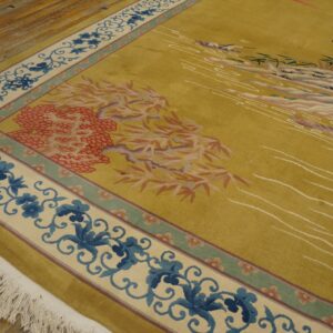 Chartreuse rug with blue scroll borders and pictorial scene laid on distressed plank hardwood flooring.
