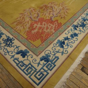 Mustard yellow rug featuring a border of blue floral vines and Greek keys resting on rustic wood floors.