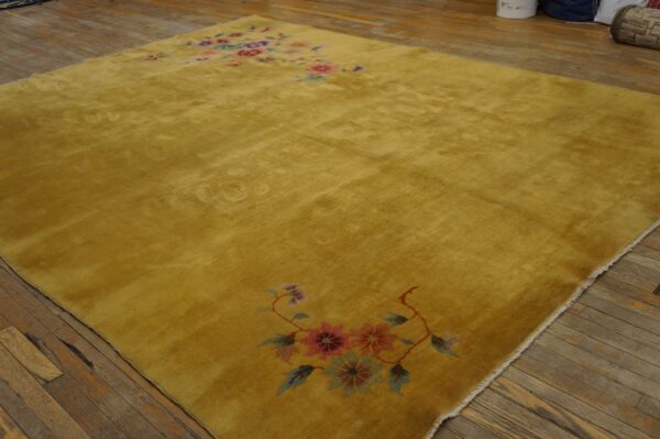 A golden-yellow high-pile rug with colorful pink and purple floral motifs lays on distressed wooden floorboards.