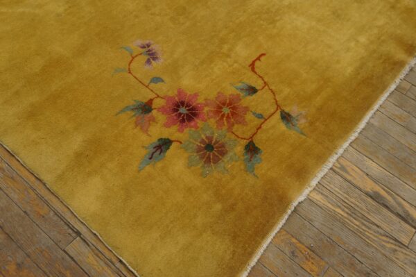 Mustard yellow rug with pink and green floral motif borders distressed brown plank flooring.