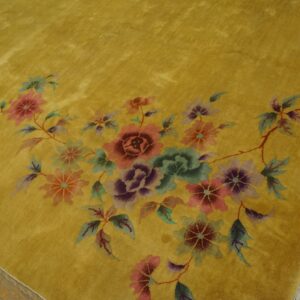 Golden yellow high-pile rug displays an arrangement of pink, purple, and green flowers on wood flooring.