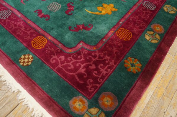 Plush teal rug with a patterned magenta border and symbolic motifs rests on light hardwood flooring.