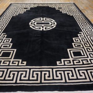 Black plush rug featuring a contrasting cream geometric border and medallion on a distressed wood floor.