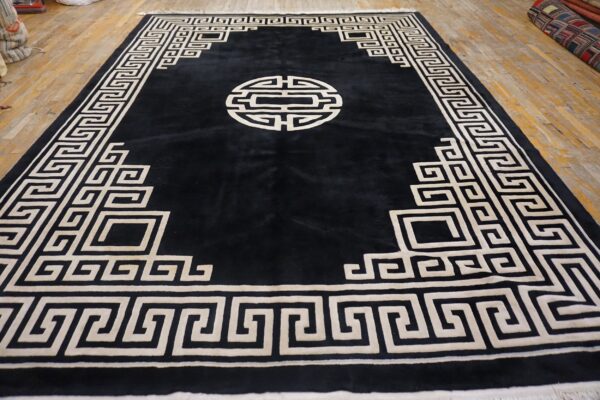 Black plush rug featuring a contrasting cream geometric border and medallion on a distressed wood floor.