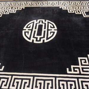 A black high-pile rug displays a cream geometric maze border and a prominent central circular motif.