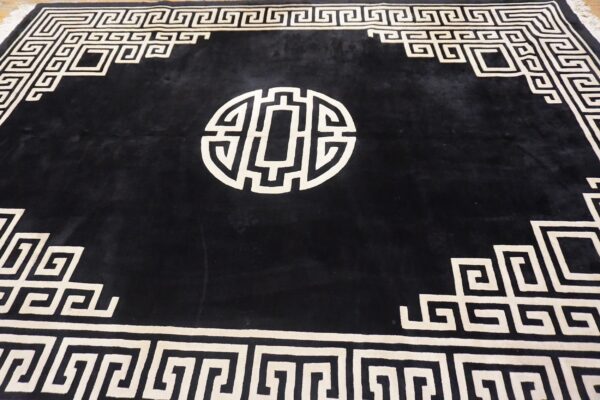 A black high-pile rug displays a cream geometric maze border and a prominent central circular motif.