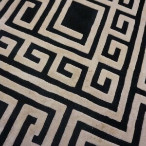 Detail of a black and tan rug featuring a large-scale, sculpted geometric maze pattern.