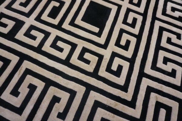 Detail of a black and tan rug featuring a large-scale, sculpted geometric maze pattern.
